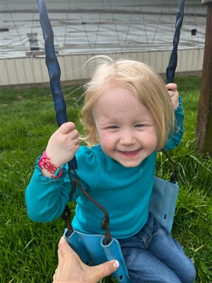 Cute young girl being pushed on a swing, with a big smile on her face, wearing a red, anchor hold fashion accessory around her right wrist.